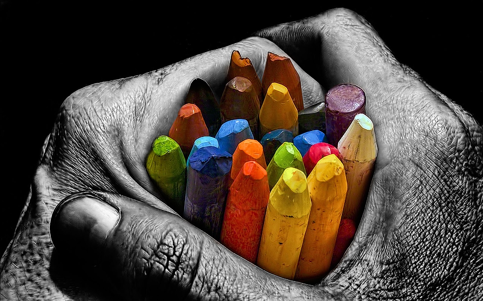 Black-and-white photograph of cupped hands holding a bundle of colorful crayons, high contrast with selective color, warm creative mood
