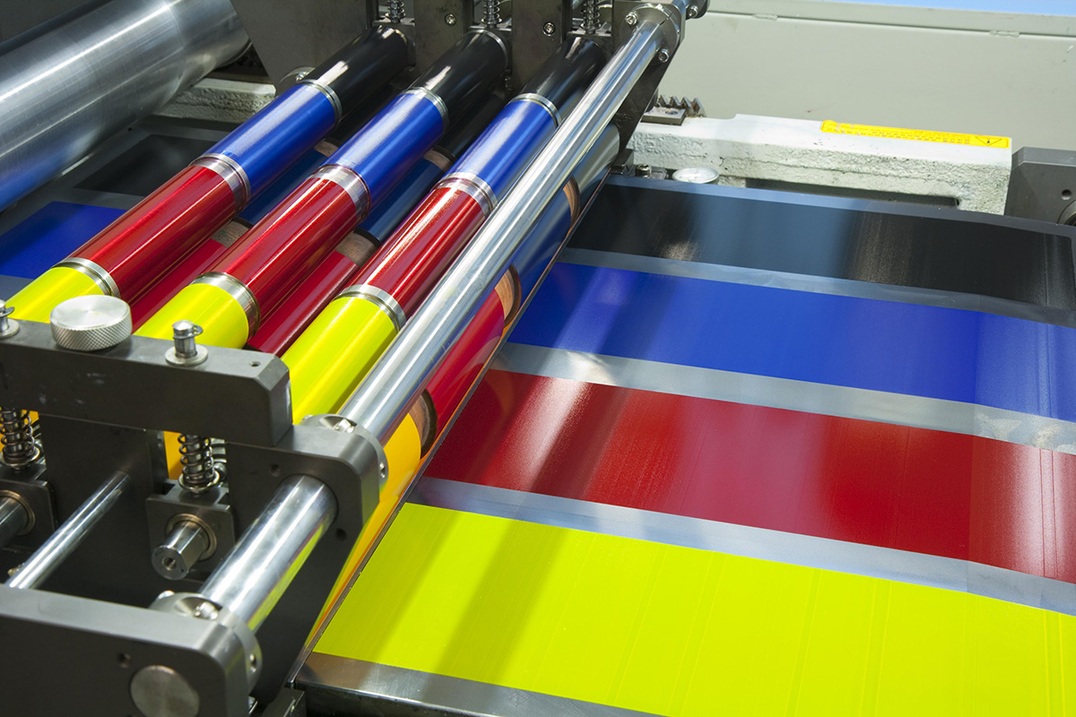 Close-up of industrial printing press rollers with cyan, magenta, yellow, and black ink on striped material, warm and vivid tones